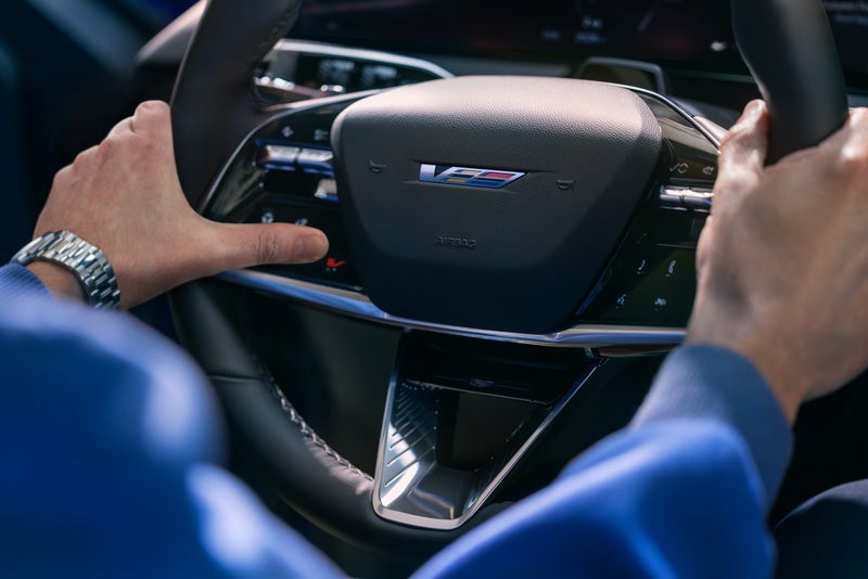 Close-up of a Man About to Press the V-Button on the 2026 OPTIQ-V Steering Wheel | Joe Cooper Chevrolet in Shawnee OK